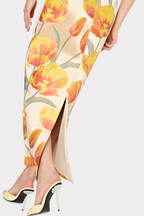 A strapless maxi dress with a floral pattern featuring primarily yellow and orange tulips on a beige background.